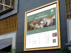 Eine Bautafel-Werbung, die die Immobilie „Am Wildbach“ an der Seite eines Gebäudes zeigt.